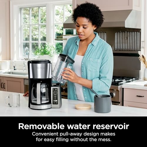 Woman using coffee maker with removable water reservoir in a kitchen.