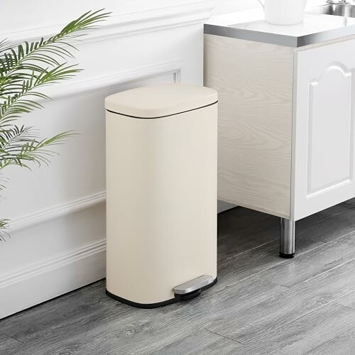 Cream-colored kitchen trash can with a foot pedal next to a counter.