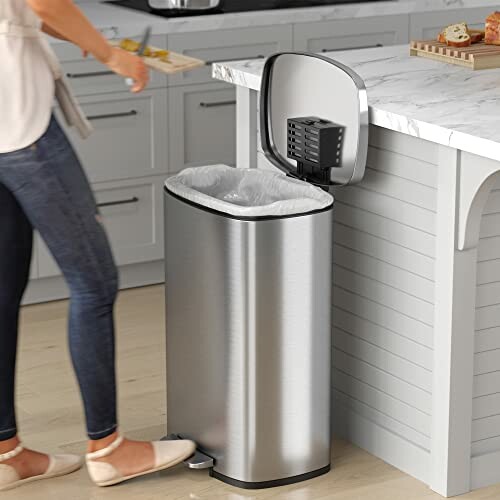 Person using stainless steel trash can in kitchen.