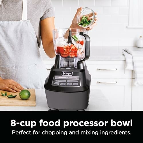 Person adding ingredients to Ninja food processor in kitchen.