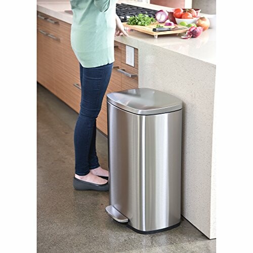 Person using a stainless steel kitchen trash can with foot pedal.